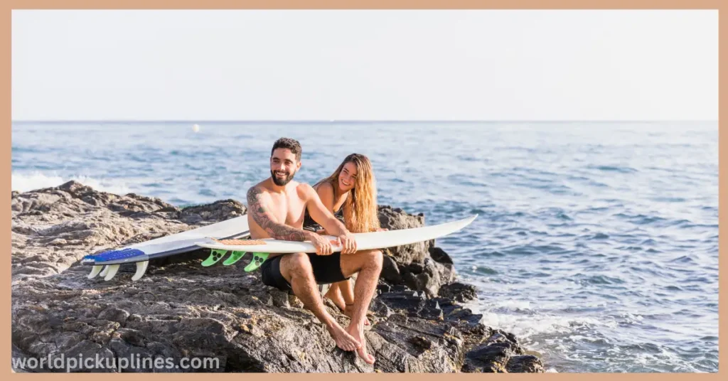A man and woman sitting on a rocky shore by the ocean with their surfboards, smiling together in the sunlight.