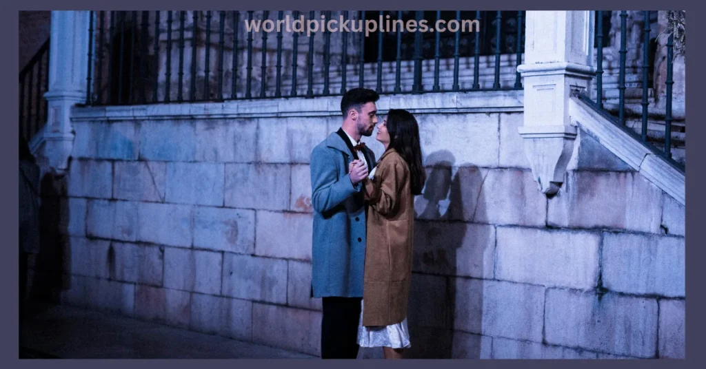 A couple in coats dancing closely outside at night against a stone wall.