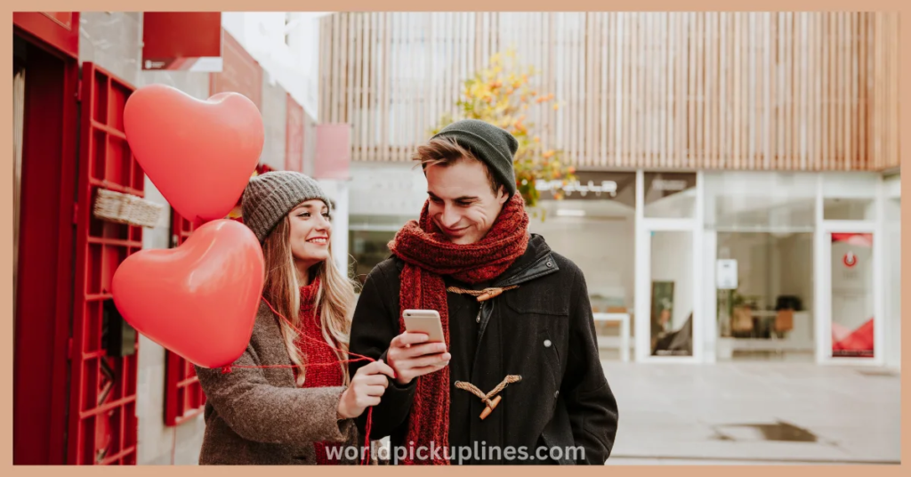 A smiling young couple in winter clothes outdoors, looking at a smartphone while holding two red heart-shaped balloons.