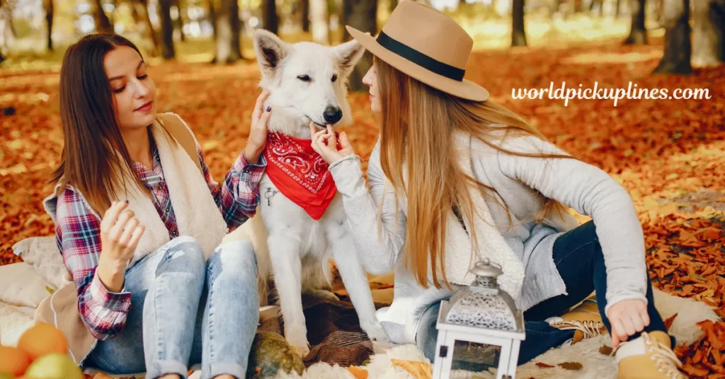 Two young women sitting on a blanket covered in autumn leaves, feeding a treat to a white dog wearing a red bandana, with "worldpickuplines.com" overlayed in the top right corner.